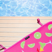 A vibrant pink, fade-resistant Margaritas Poolside Seating Mat with lime and cocktail print resting beside a swimming pool, suggesting a fun and relaxing tropical vacation vibe by Emerson West.