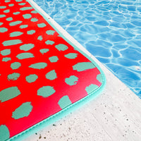 A quick-dry, Pink Cheetah Poolside Seating Mat by Emerson West next to a pool.