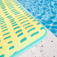 A brightly colored Emerson West neon yellow poolside seating mat resting on the edge of a swimming pool with crystal clear blue water, hinting at leisure and relaxation on a sunny day.