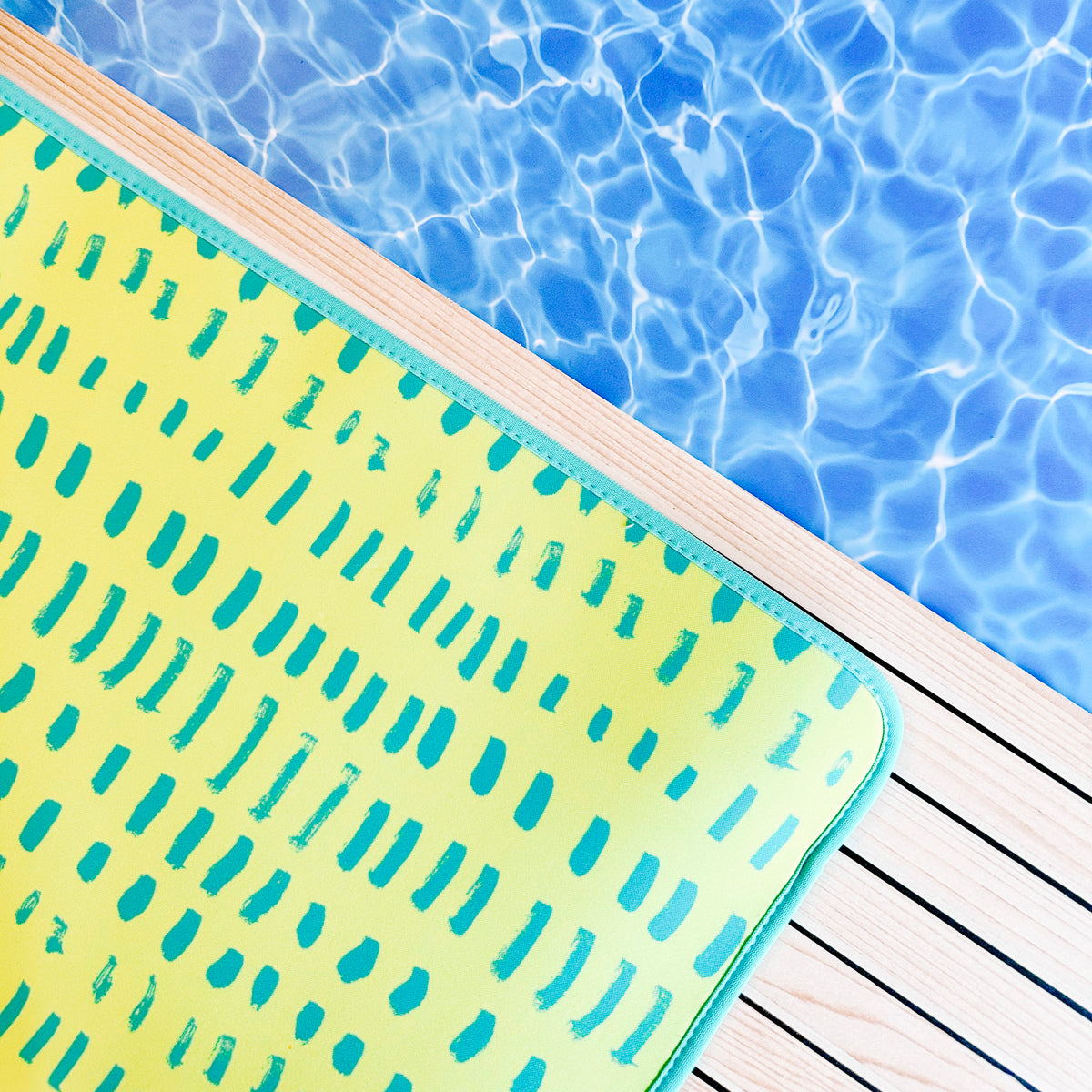 A brightly colored, fade-resistant Emerson West Neon Yellow Poolside Seating Mat resting on the edge of a swimming pool with clear blue water.