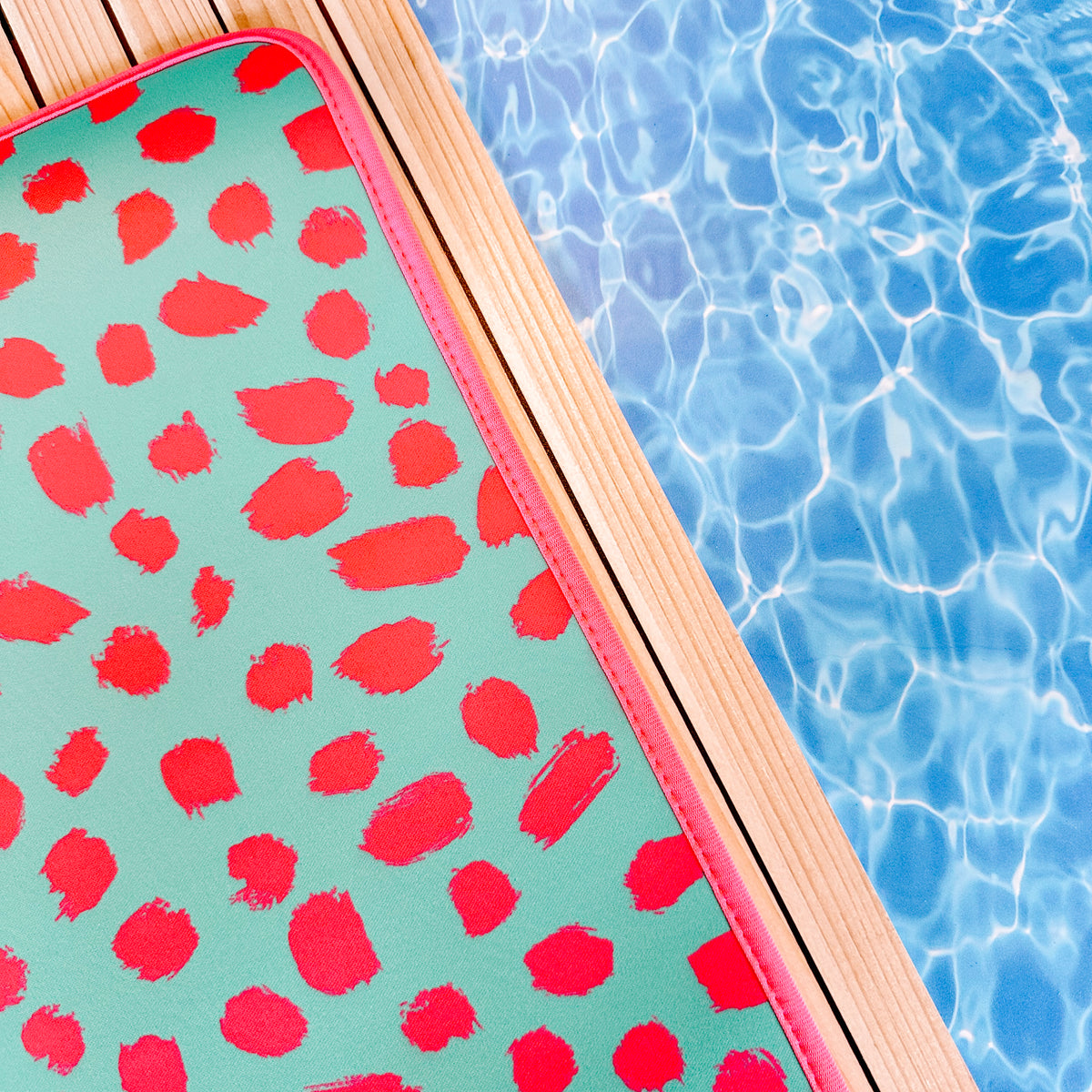 A Teal Cheetah Poolside Seating Mat by Emerson West on a surface next to a pool.