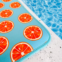 A vibrant pool seat designed with orange slice graphics rests at the edge of a sparkling swimming pool, inviting summer fun. This Emerson West Oranges Poolside Seating Mat is fade-resistant, ensuring its bright colors remain vivid all summer.