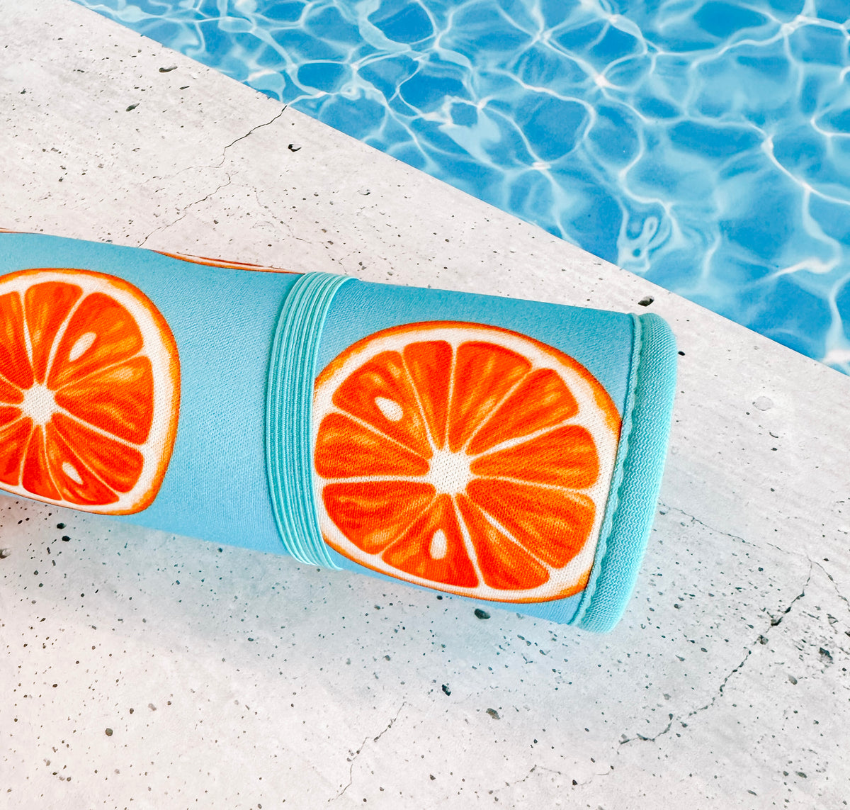 A colorful, fade-resistant Oranges Poolside Seating Mat by Emerson West rolled up beside a swimming pool, capturing a refreshing and vibrant vibe for an outdoor fitness or relaxation session.